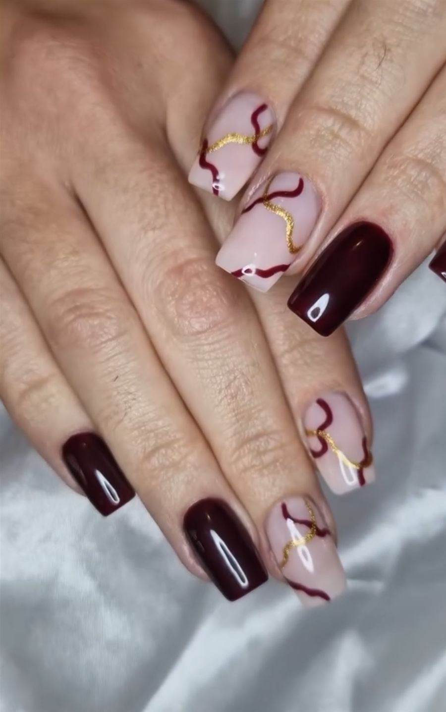 Ongles carrés bordeaux et nude, arabesques bordeaux et dorées